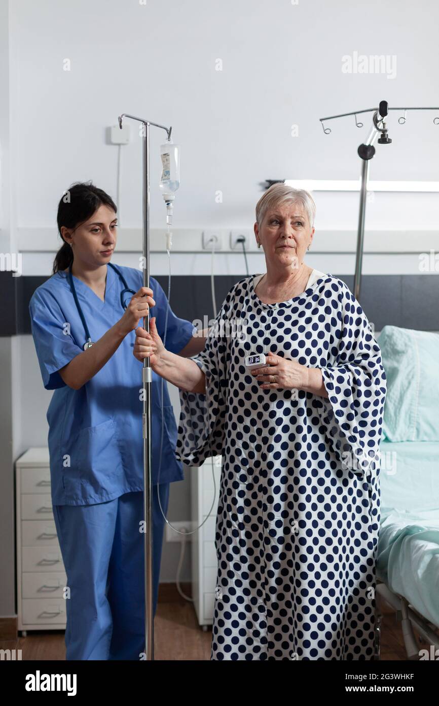 Nurse Dressed With Scrubs Helping Senior Woman Patient With Iv Drip Bag